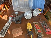 Workshop tools on table showing swivel riveter, retaining ring pliers kits, three lights, saw with miter box, and wooden box with plastic storage bin in background.