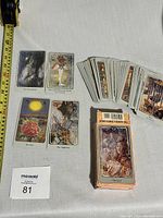 Photo showing spread of several tarot cards from the deck along with stack of remaining cards and original box placed on flat surface.