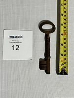 Full view of the antique wrought iron key next to a measuring tape showing it is about 11 cm long.