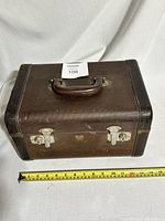 Closed small brown vintage Mid Century Modern suitcase with metal clasps and handle, accompanied by measuring tape for scale showing approximately 13 inches wide.