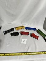 Overview of all seven HO scale train cars including locomotive, boxcars, caboose, and tanker car on white fabric background with measuring tape.