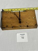 Top view of a rectangular solid oak block measuring about 12 inches with mounted lock mechanism and a pointed element at the center.