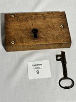 Solid oak door lock plate with attached deadbolt and keyhole, showing the key inserted and part of the lock mechanism visible on the side. Three brass screws secure the plate.