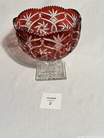 Side view of the large cranberry cut glass pedestal footed bowl showing the intricate star and geometric cut patterns on cranberry red glass with a clear square pedestal base.