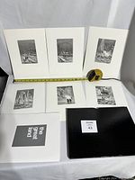 Six black and white engraving prints laid out with measuring tape and portfolio folder.