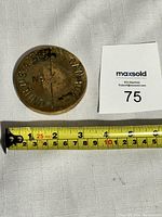 Top side of circular brass border marker with border marking and number