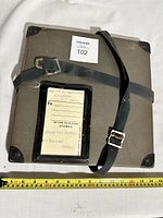 Top view of the vintage metal film reel case showing shoulder strap, corner protectors, and attached card holder with label.