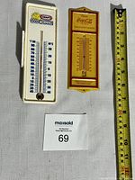 Two thermometers side by side with a measuring tape for scale, Kraft on the left and Coca-Cola on the right.