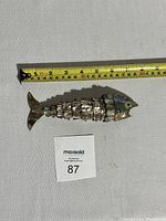 Full view of the articulated fish-shaped bottle opener placed next to a measuring tape showing about 8.5 inches length.