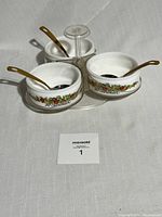 Front view of the spinning condiment tray showing three white ceramic bowls with floral design and gold spoons.
