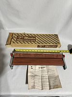 Photo showing the complete rolling machine, original box behind it, and instruction sheet placed in front, with a measuring tape indicating size.