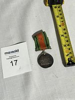 Photo of WWII Defence Medal with ruler for size scale, showing medal with orange and green striped ribbon.