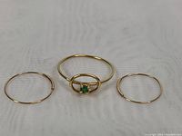 Top-down view showing ring with oval frame and emerald, flanked by two thin gold hoop earrings.