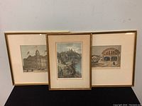 Three gold-toned framed etchings displayed side-by-side showing historic city scenes and buildings.