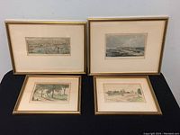 Four framed antique etchings depicting various city and rural scenes, arranged on a table.