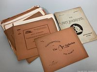 Photo showing a stack of antique art journals and photograph portfolios with visibly aged covers, titles include 'The Art Journal' and 'John L. Stoddard's Portfolio of Photographs'.