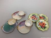 Photo showing three biscuit tray and teacup sets along with three hand-painted plates featuring floral designs and gold accents.