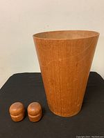 Front view of teak trash can and pair of salt and pepper shakers on black surface