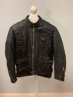 Front view of men's black leather biker jacket on display, showing zipper, pockets, and belt closure