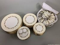 Overall view of stacked dinner plates, luncheon plates, dessert plates, salt and pepper shakers on a dessert plate, and quilted case of teacups and saucers