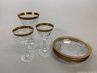 Photo showing three crystal goblets of different sizes with gold rims and four matching crystal plates with gold rims stacked.