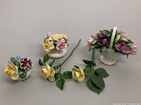 Photo showing three floral bouquets and three individual rose stems arranged on a table against a gray background, highlighting the color and detail of each porcelain flower
