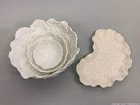 Four white ceramic leaf-themed serving pieces: one Spode leaf plate and three Coalport nesting cabbage leaf bowls.
