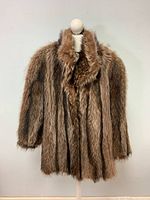 Front view of vintage raccoon fur coat on a mannequin against a plain background showing its shape and fur texture.