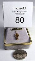 Front view of the 10KT gold lapel pin in a gray display box with a coin for scale.