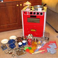 Wide view of red Brio child's toy stove and oven with included kitchen play pieces laid out in front on carpet.