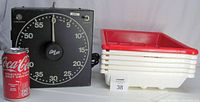Photo showing Gra Lab 300 timer with large dial and knob next to stack of six Paterson developer trays with red rims with soda can for scale