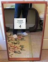 Full view of the teak framed Mid-Century Modern mirror reflecting a floral rug and surroundings, showing the frame and overall shape.