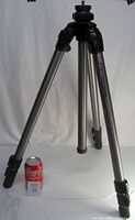 Front view of tripod with extended legs next to a soda can for size reference, showing aluminum legs and black locks.