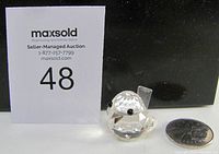 Front and side view showing the clear faceted crystal bird with black eyes, small size relative to coin, and detailed shape.