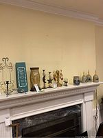 Wide view of mantle displaying assorted candle holders, pottery jars, and metal wall sconce.