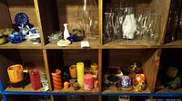 Shelves with assorted candles in multiple colors including orange, yellow, red, pink, alongside various glass candle holders and decorative ceramic items.
