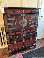 Front view of the ornate wooden chest showing five small top drawers, two large central cabinet doors with metal hinges and latch, and two lower drawers with metal handles.
