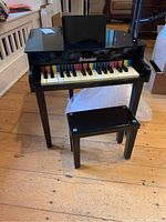 Front view of Schoenhut child piano with bench on wooden floor, showing keyboard and brand name on piano front.