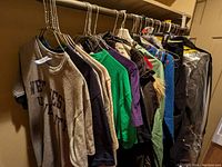 View of assorted clothing items on hangers including t-shirts, jackets, and blouses.