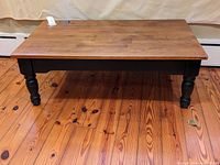 Full front view of wood coffee table showing top and turned legs on wood floor.