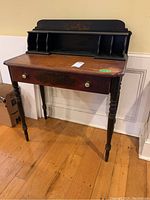 Full view of small wooden secretary desk showing top surface, drawer, turned legs, and upper cubby storage section.