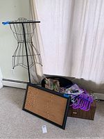 Photo showing black wire dress form, cork bulletin board, fabric covered hangers, storage bags and box arranged on floor near window with beige curtain.