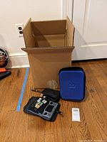 Overall view: cardboard box, blue and black cases, console, chargers, cartridges scattered