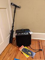 Ion Tailgater portable sound system with microphone mounted on adjustable tripod stand, extension microphone cable, and packaging on floor.