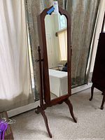 Full view of cherry wood full length mirror standing upright showing its arched top and legs.