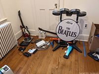 Wide room shot showing drum kit on stand, two guitar controllers, Wii console, balance board, games stack
