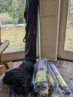 Full view of the black volleyball net in a carrying bag, along with two packaged garage door screens rolled in plastic.