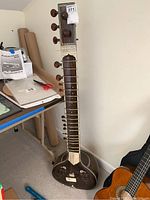 Full view of sitar showing long neck with tuning pegs, body shape, and overall condition including missing piece on bridge area.