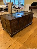 Front angle view of the wooden coffee table with sliding top and carved panel details on the side.