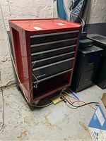 Front angle view of red Craftsman metal toolbox in basement with visible drawers and wheels.